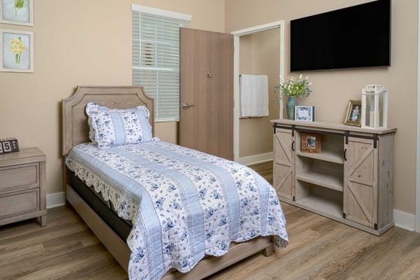 A cozy bedroom featuring a bed, bedside table, and TV in The Willows of Jackson.