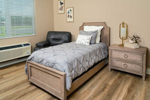 A furnished bedroom with a bed, recliner, and nightstand.