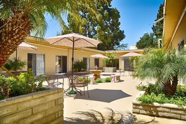 Sunny courtyard with tables, chairs, and umbrellas at Ventura Post Acute.
