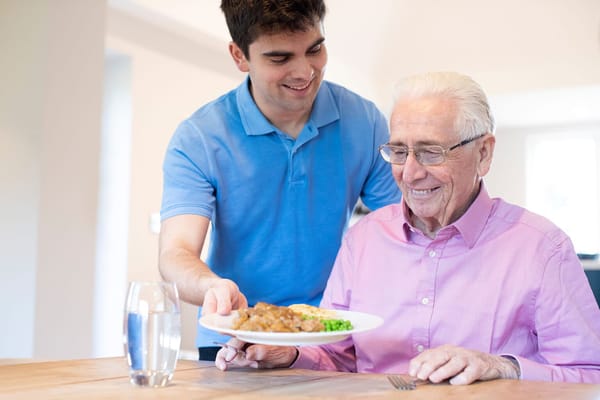 Staff serving a meal to a smiling resident