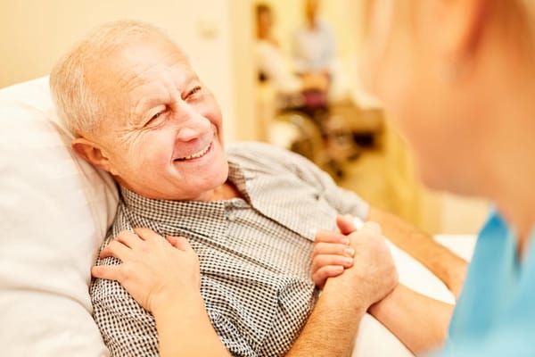 A caregiver holding hands with a smiling senior resident