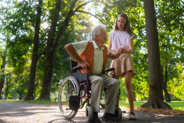 An elderly man in a wheelchair enjoying time outdoors with a young woman