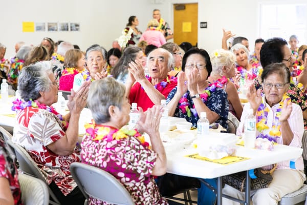 Residents celebrating with leis and food at a dining area
