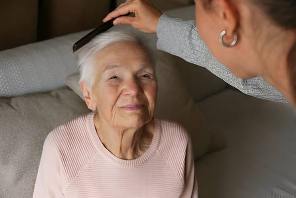 Caregiver brushing an elderly woman's hair indoors