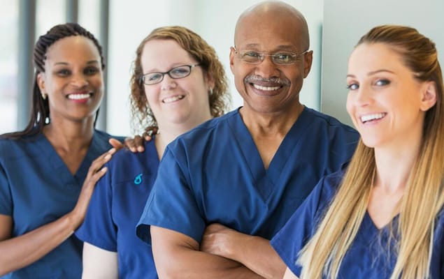 Four healthcare professionals smiling in scrubs
