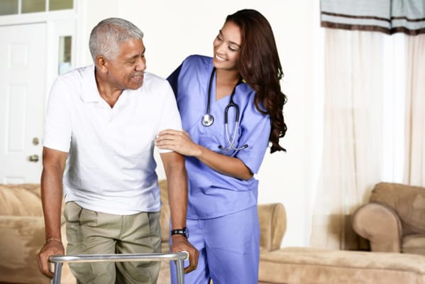 Nurse assisting a senior man with a walker in a cozy living room