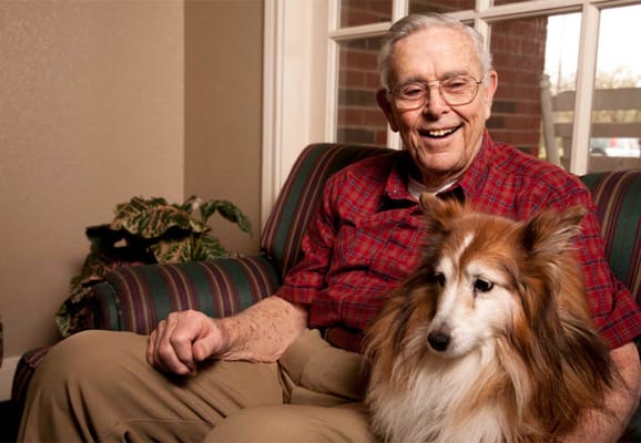 An elderly man smiling with a small dog on his lap