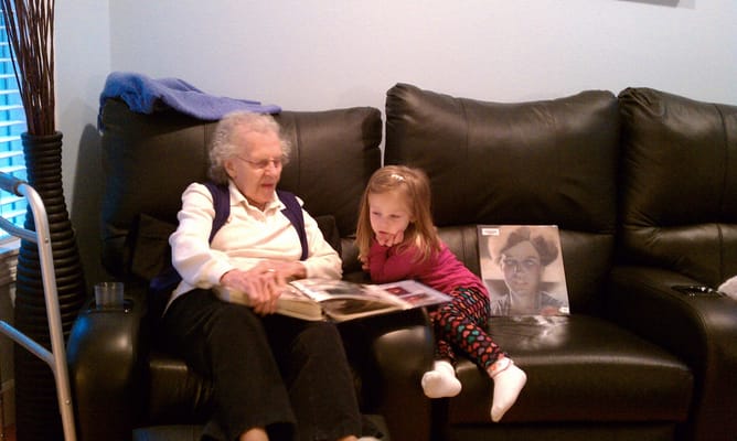 An elderly woman reading a photo album with a young girl