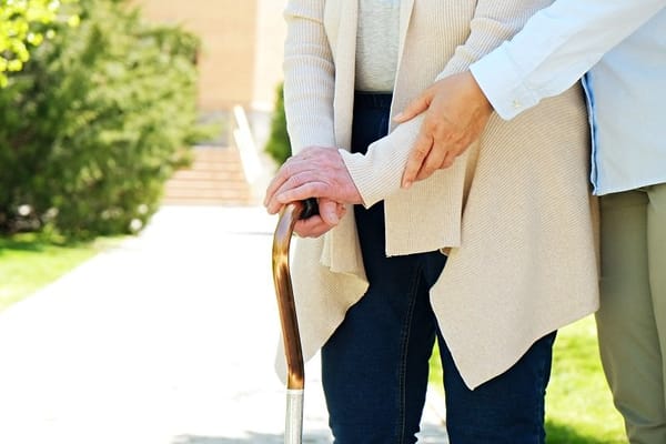 Resident receiving assistance outdoors with a cane
