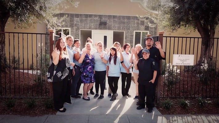 Staff members waving in front of the facility entrance