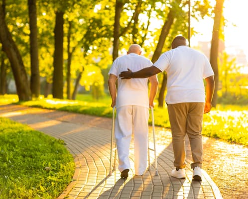 Caregiver assisting a resident on a sunny path