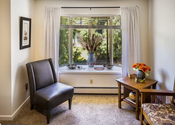 A cozy living room featuring a chair, a window with a view, and decorative items on a table.
