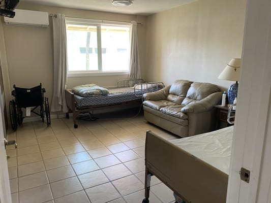 Interior view of a resident room with a hospital bed, couch, and wheelchair.
