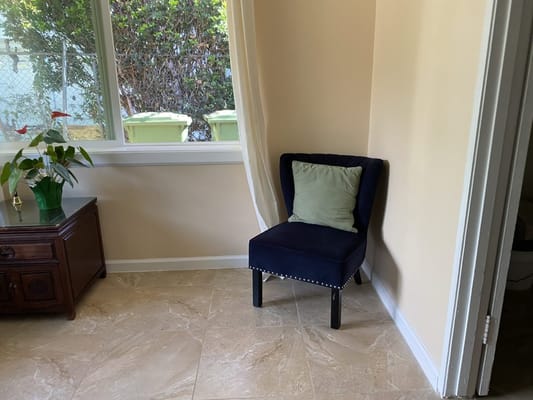 A cozy lounge chair with a green cushion next to a wooden cabinet and a flowering plant.