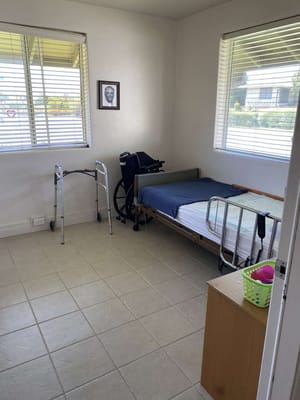 A small bedroom with a hospital bed, walker, and a chair