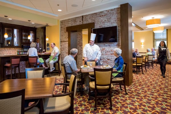 Residents enjoying a meal in the dining area with a chef and staff.