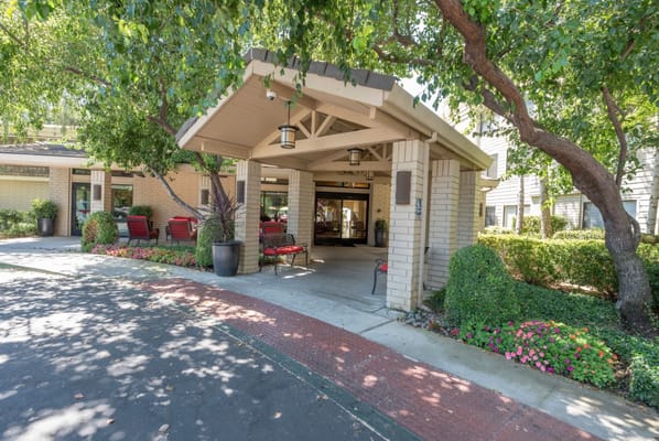 Entrance of Campus Commons Senior Living surrounded by greenery and flowers.