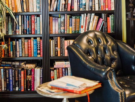 A black leather armchair next to a bookshelf filled with colorful books.