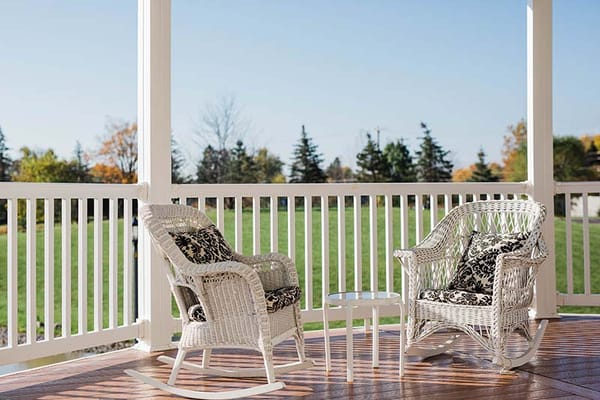 Two white wicker chairs with black and white cushions on a porch