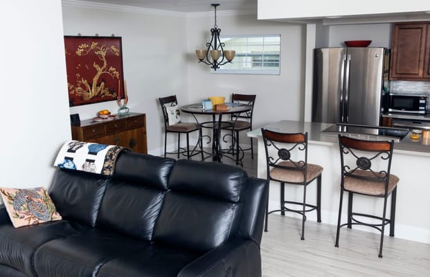 A comfortable living area with a black sofa, dining table, and modern kitchen appliances.