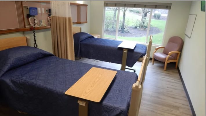 A private resident room with two beds and a chair