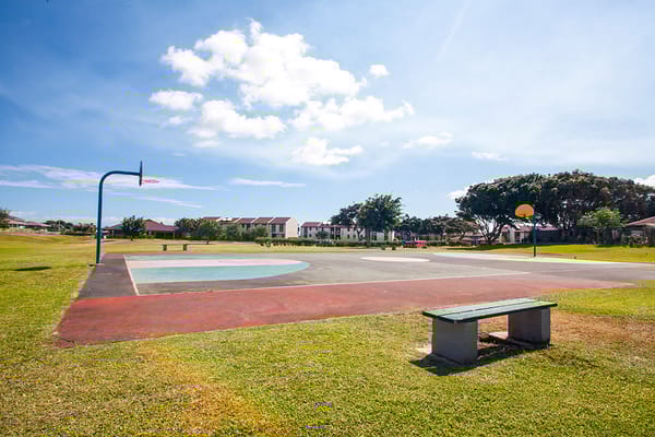 Open basketball court with a bench and residential buildings in the background