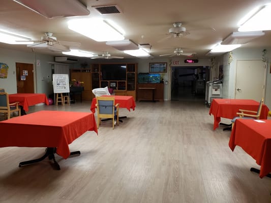 Interior view of a common area with red tablecloths and wooden chairs.