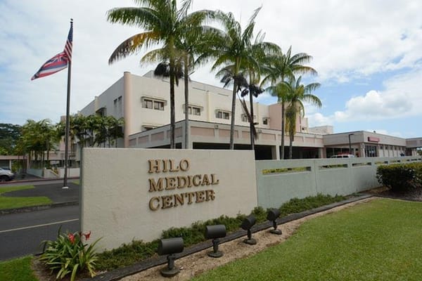 Exterior view of Hilo Medical Center with palm trees and American flag.