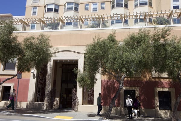 Front entrance of Rhoda Goldman Plaza with trees and people walking by.