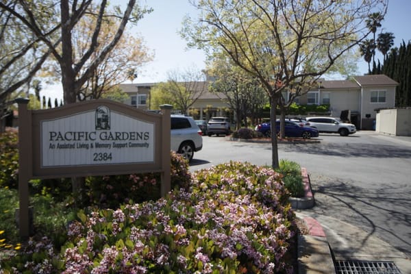 Exterior view of Pacific Gardens with flowers and signage