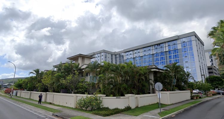 Exterior view of Kaluanui Senior Apartments with palm trees and cloudy sky.
