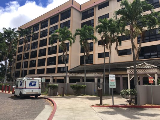 Exterior of Kamalu Hoolulu Elderly Housing with palm trees and a USPS vehicle