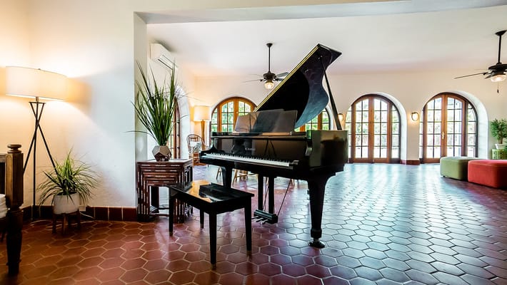 A grand piano with a small bench in a spacious lobby area with natural light.