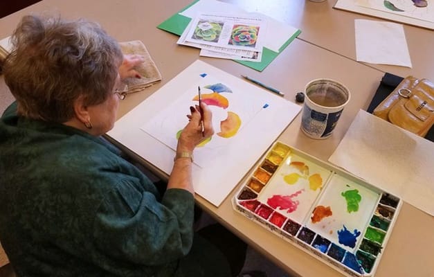 Senior resident painting at a communal table