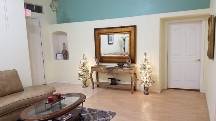 A cozy living room featuring a mirror, decorative furniture, and small Christmas trees.