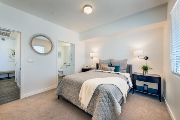 Finished bedroom with gray bedding and a decorative headboard.
