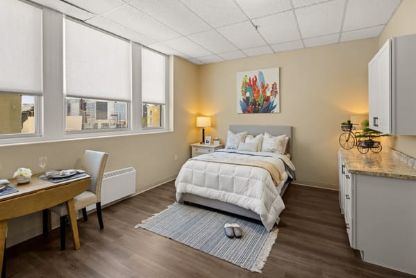 Bright and cozy bedroom in a senior living facility with a bed and a small dining table.