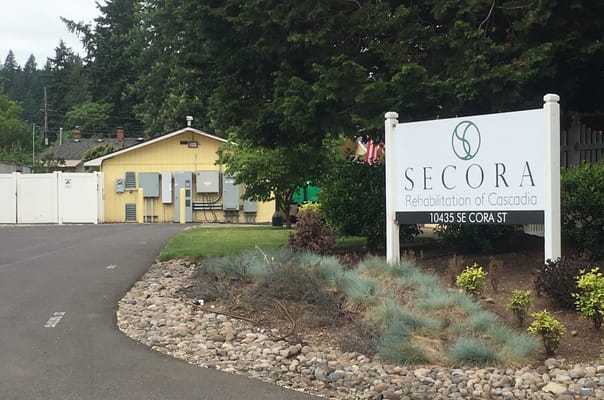Entrance sign for Secora Rehabilitation of Cascadia with a yellow building in the background