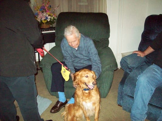 An elderly man enjoying time with a golden retriever in a cozy living area.
