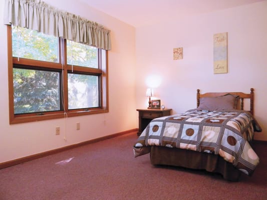 A cozy bedroom featuring a bed with a patterned blanket, a bedside table, and large windows.