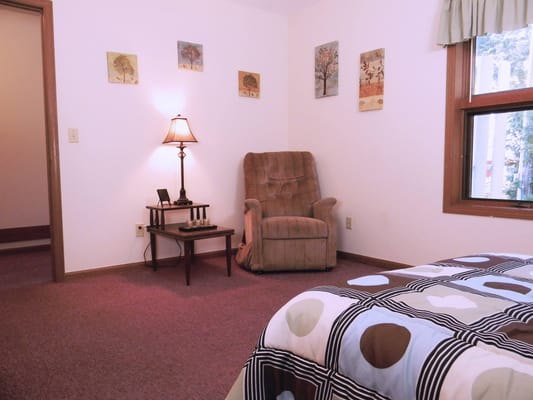 A cozy bedroom with a chair, lamp, and artwork on the walls.