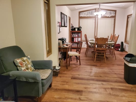 View of a living and dining area with a comfortable chair and wooden dining table.