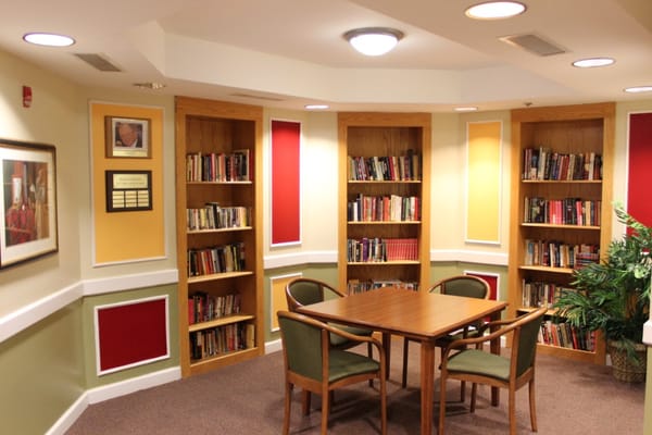 Library corner with bookshelves and a table in a senior living facility.