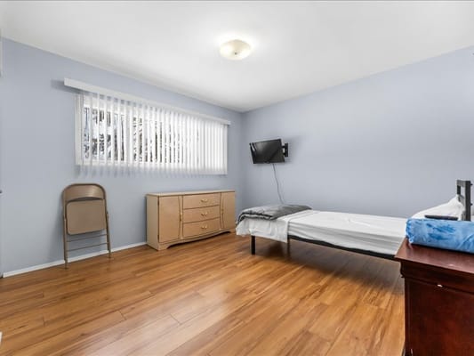 A simple bedroom with a bed, dresser, chair, and TV.