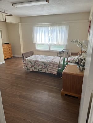 A cozy bedroom with a floral bedspread, dresser, and large window.