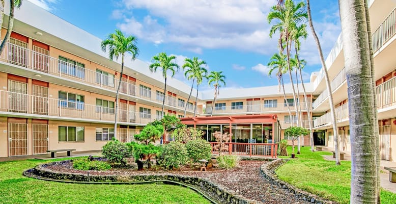 Lush courtyard with palm trees and garden at Waipahu Hall Elderly Apartments