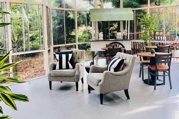 Sunroom with two chairs and tables surrounded by greenery.