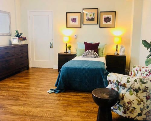 A bright and inviting bedroom with a bed, dresser, and floral accent chair.