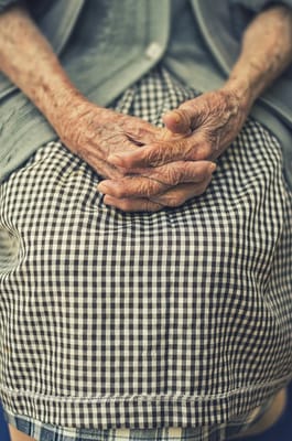 Close-up of elderly hands resting on a checkered apron