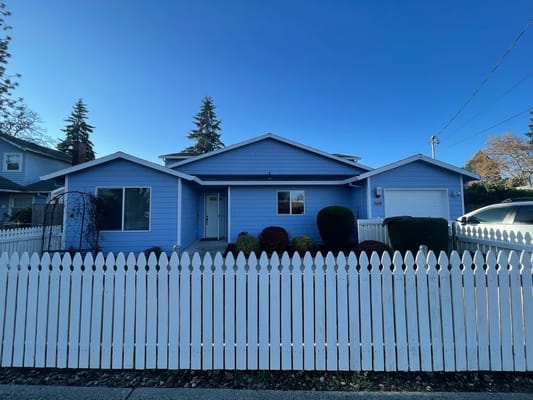 Front exterior of a single-story blue house with white fence